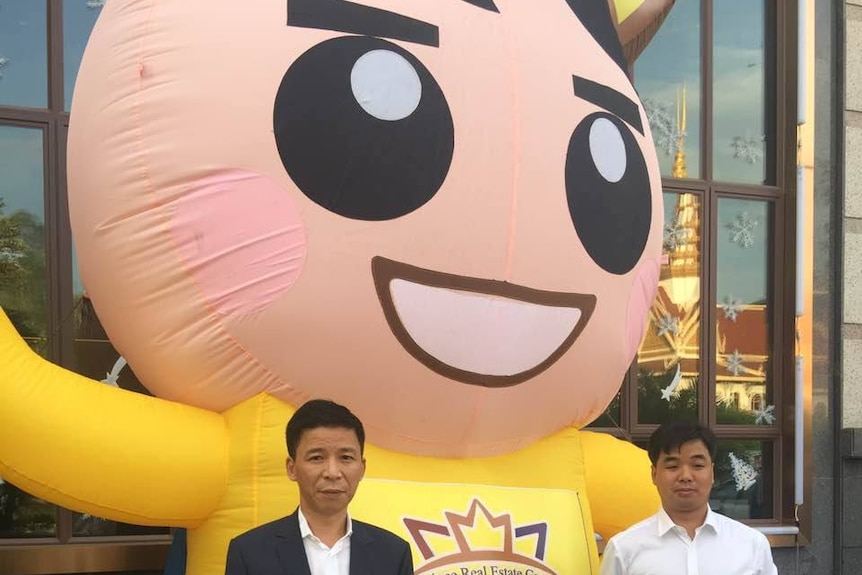 Two men stand in-front of a giant inflatable cartoon prince.