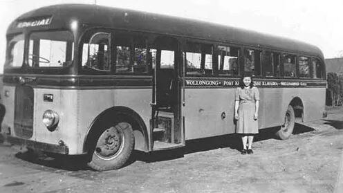 A black and white picture of an old 1940s bus with a woman standing nearby.