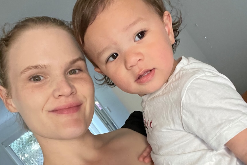 a mother holds her toddler, smiling into the camera