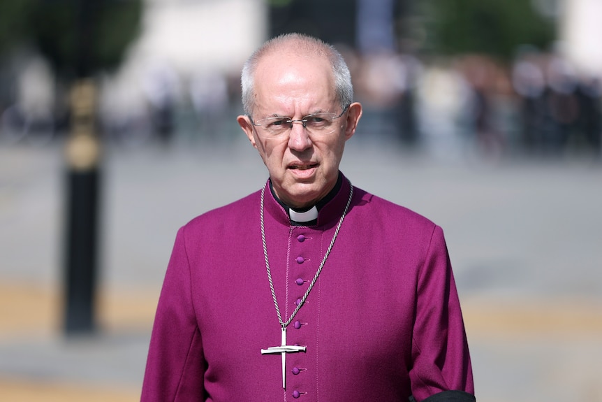 The Archbishop of Canterbury Justin Welby wears a purple top and chain with a cross as he walks in Westminster