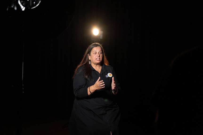A woman being interviewed in a dark room. 