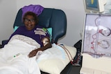 An Indigenous woman in a dialysis chair receiving dialysis with a pump to her side.