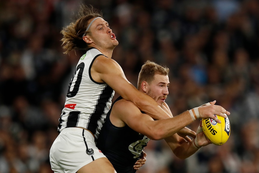A Carlton AFl player marks the ball in front of a Collingwood opponent.