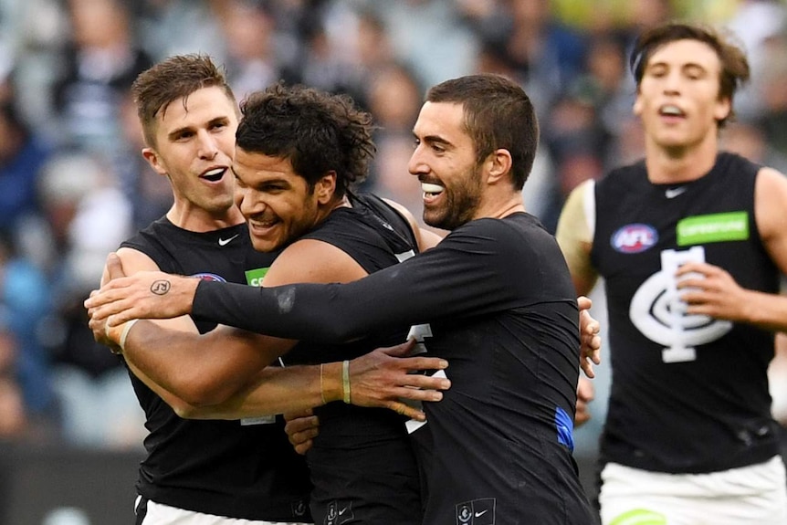 Three men in black and white football uniforms hug on the field.