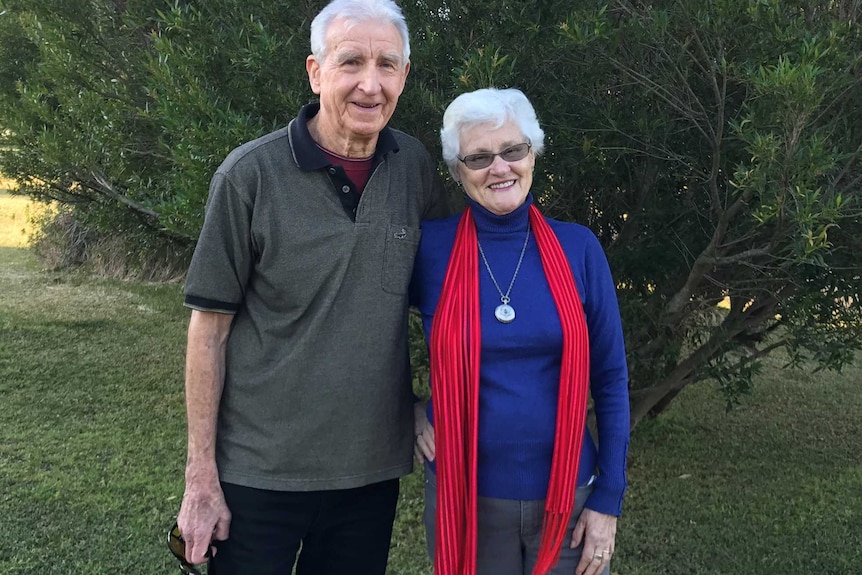 A man and a woman stand in front of a tree.