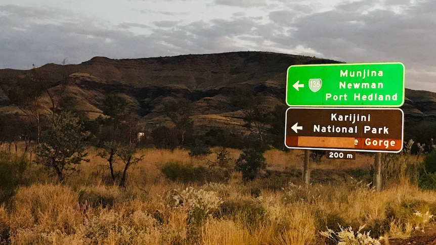 Landscape image of a road, with a sign pointing to Karijini National Park.