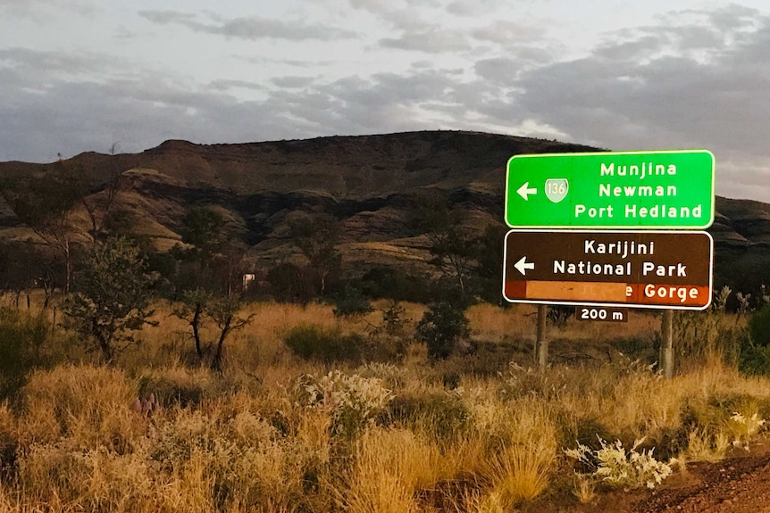 Landscape image of a road, with a sign pointing to Karijini National Park.