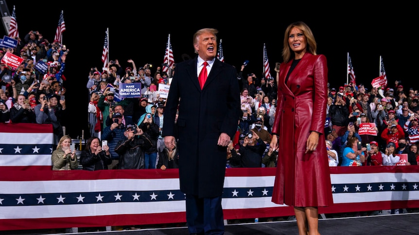 You view Donald Trump and Melania Trump on a rally stage at night.