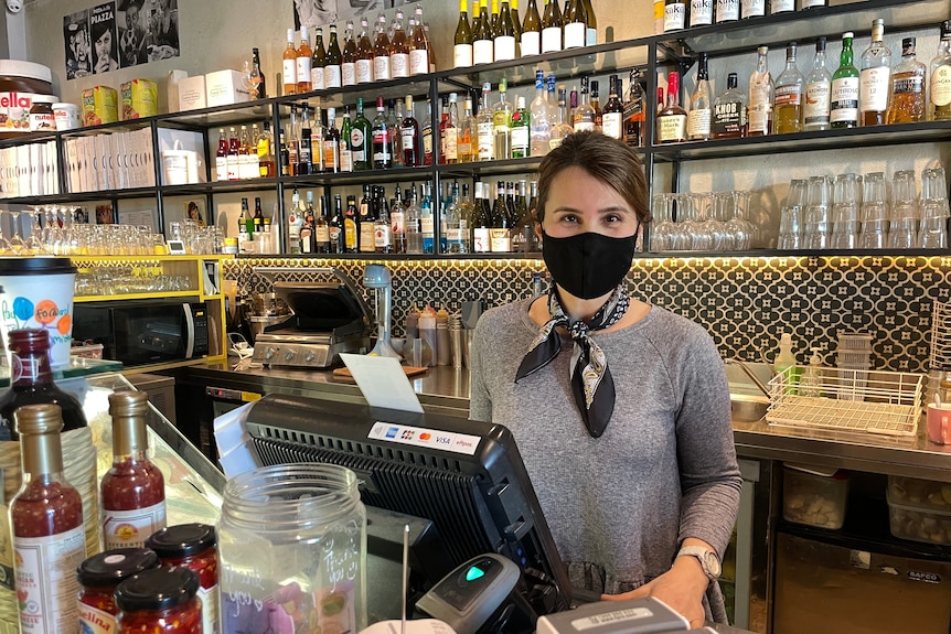 A woman in a mask standing in front of a cash register and bar