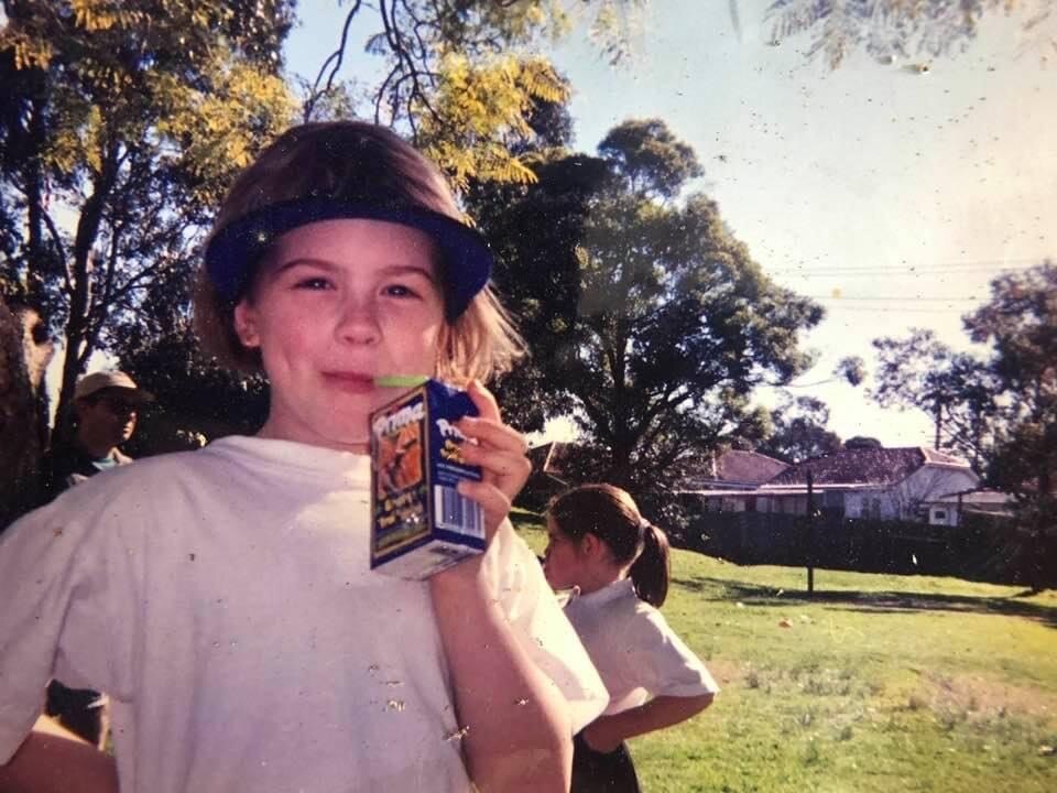 An old photo of Josie Bober when she was a young child, looking into the camera and drinking a box of juice.