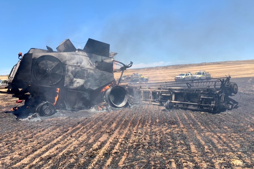 A harvester sits charred and crumpled by fire in a burnt grain paddock