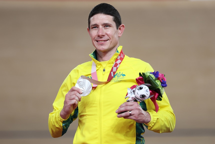 An Australian male cyclist smiles as he holds his Tokyo Paralympic medal on the podium.