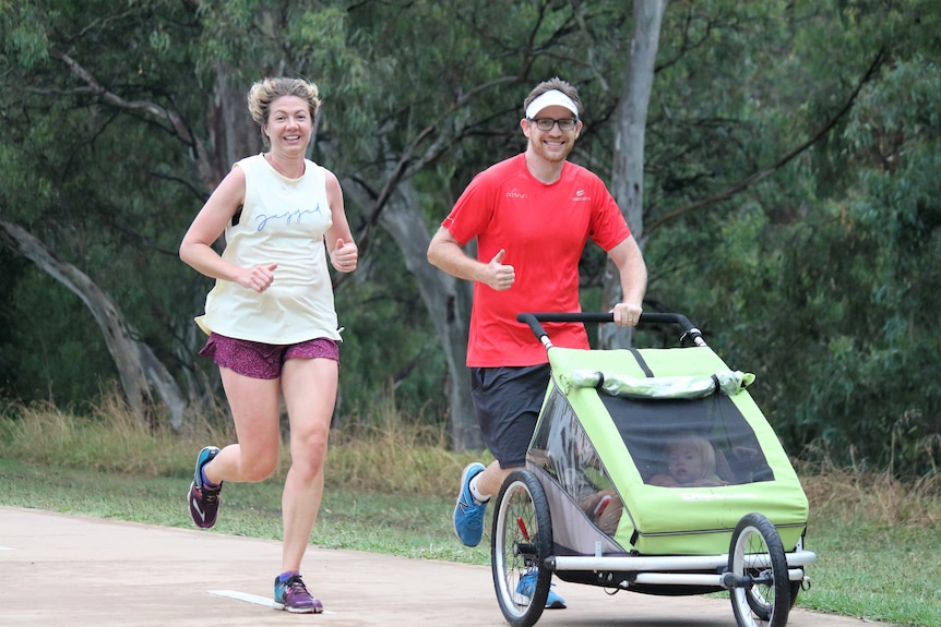 A couple run with kids in a running buggy at parkrun.