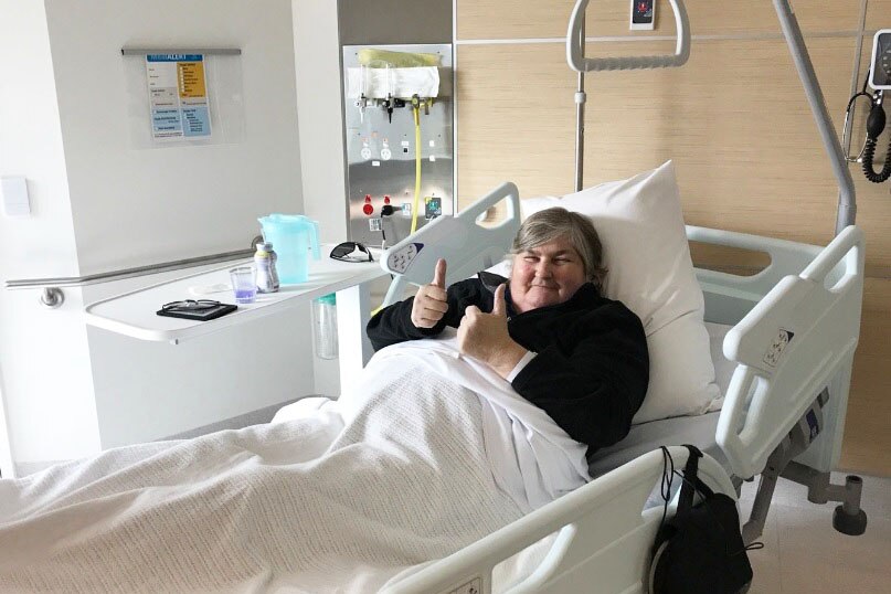 A patient gives the thumbs up with both hands from her hospital bed.