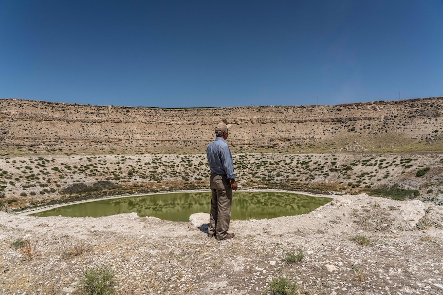 A man stands next to a large sinkhole filled with greenish water