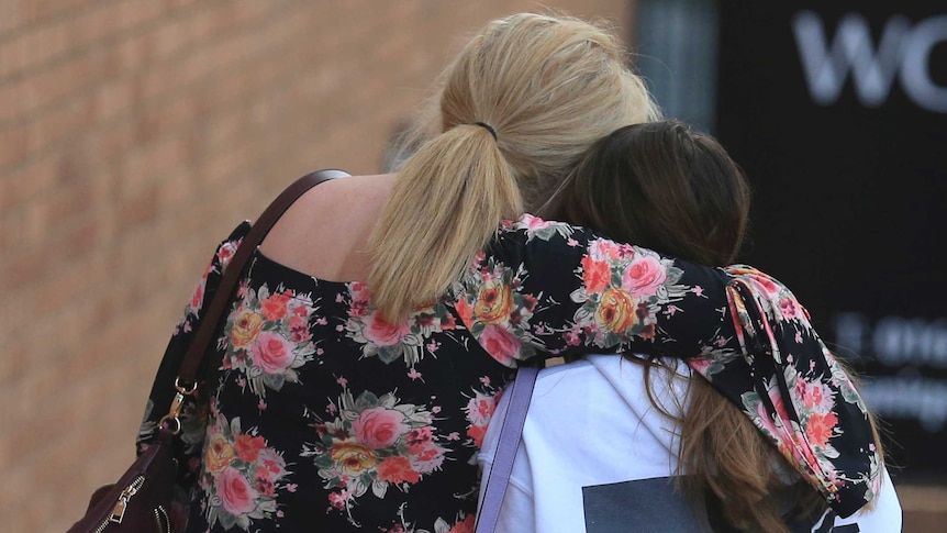 A mother in a floral shirt holds her daughter as they walk down the street of manchester