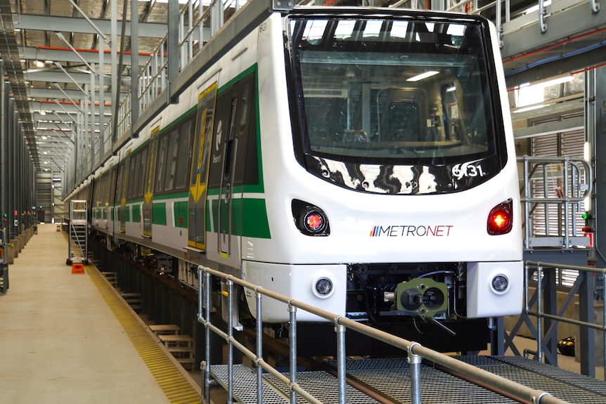 New white train with green stripes being built at a railcar manufacturing facility.