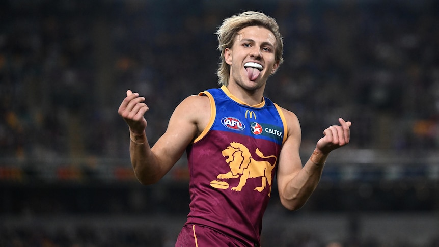 A Brisbane Lions AFL player grins with his tongue out as he celebrates during a game.