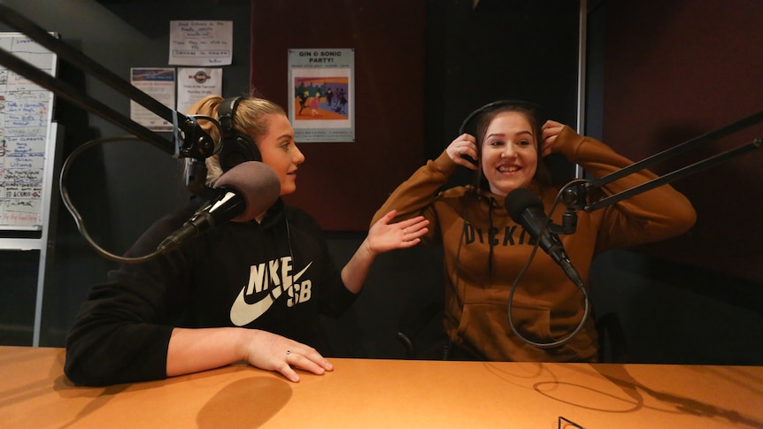 Jesse and Tegan, both wearing headphones share a joke.