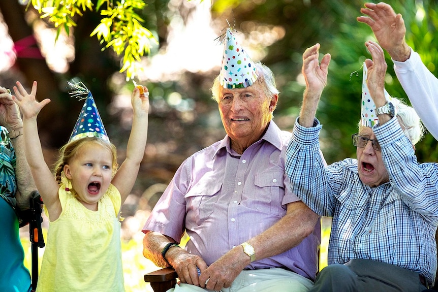 An elderly man in a party hat throws up his hands with a young girl on the ABC TV series Old People's Home For 4 Year Olds.