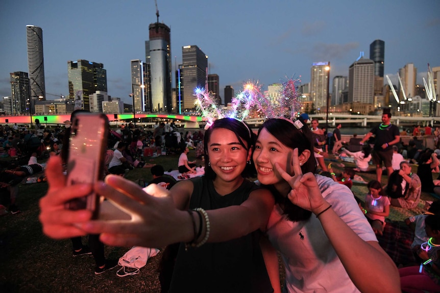 Two women take a photo on  mobile phone on Brisbane's Southbank waterfront