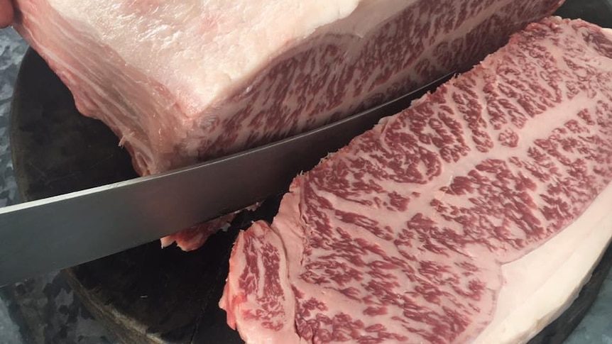 A very marbled piece of steak being sliced on the butcher's block.