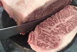 A very marbled piece of steak being sliced on the butcher's block.