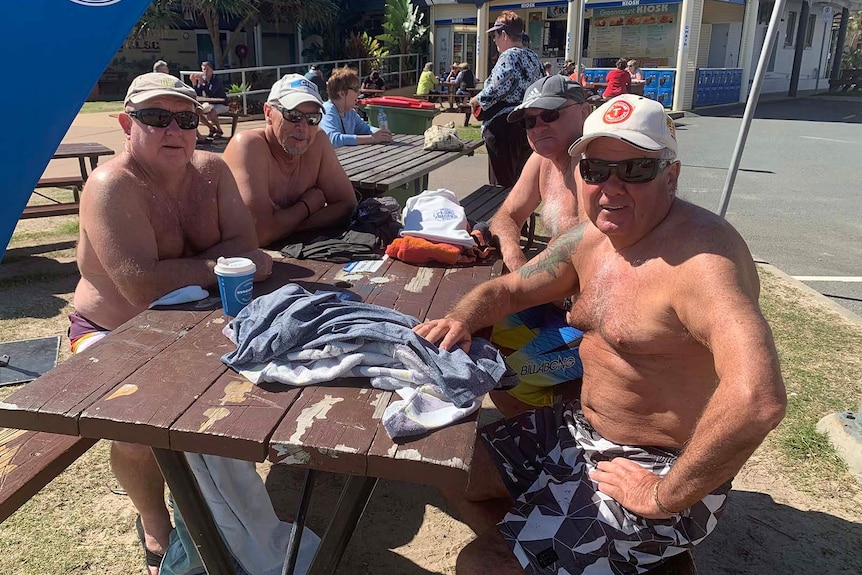 A group of men sitting at a beachfront picnic table