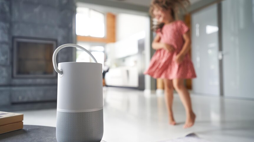 A young girl in a pink dress dances against the background of a remote Wi-Fi Smart speaker