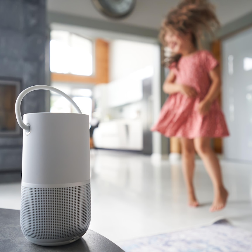 A young girl in a pink dress dances against the background of a remote Wi-Fi Smart speaker