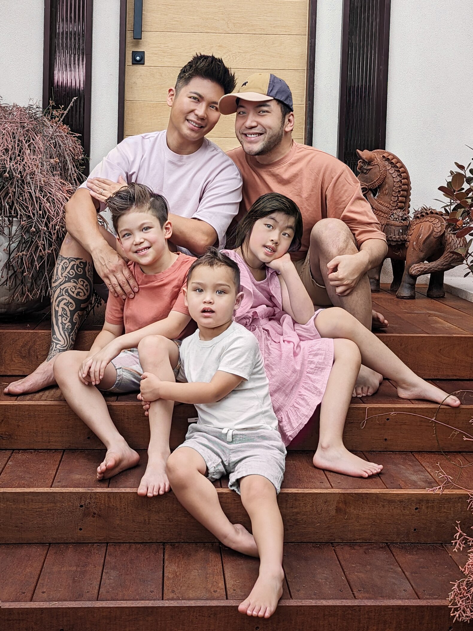 Two men and three kids sit together on a stoop, laughing with arms around one another.