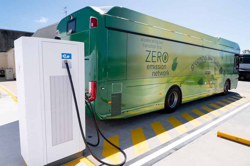 An artist's impression of an electric bus being charged by a white rectangular charging station.