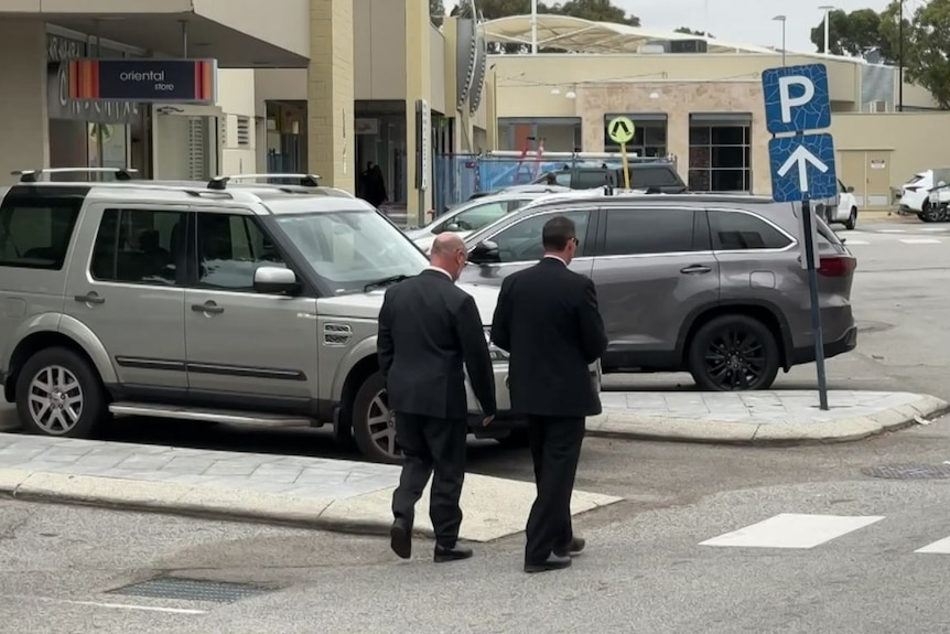 Two men in suits walking through a shopping centre car park.
