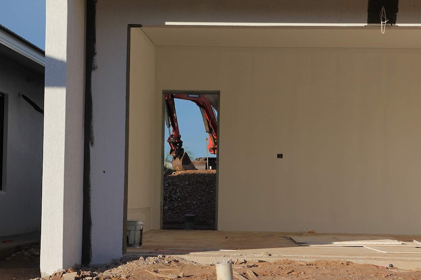 A view of a red crane visible through the door of a half-built house.