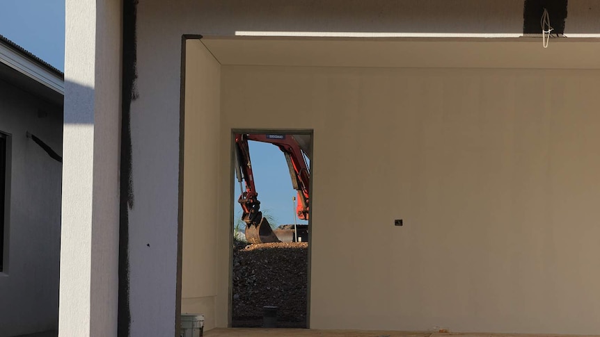 A view of a red crane visible through the door of a half-built house.