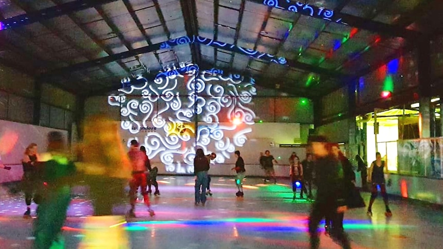 Wide photographic shot of blurry figures on a roller skating rink with disco lights