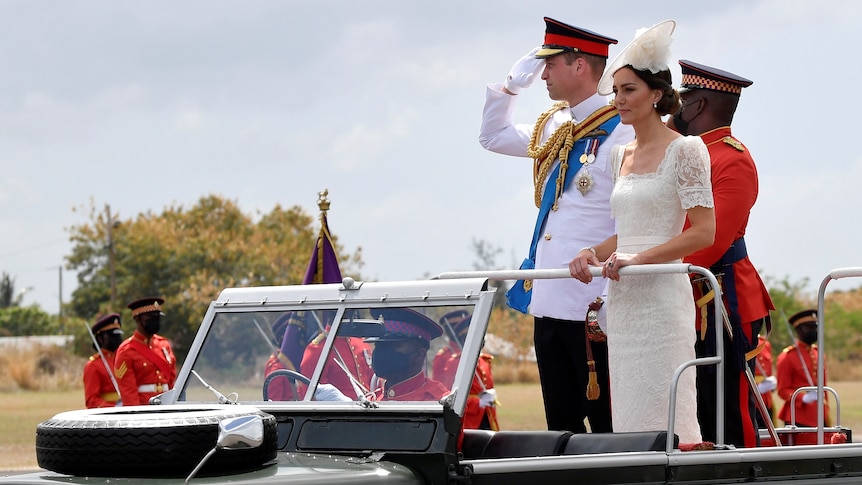 Prince William in military uniform and Catherine stand up in the back of aLandRover with the top down.