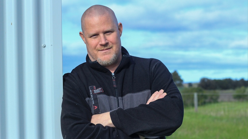 Portrait of Mark Pember leaning against a fence with arms folded outside 