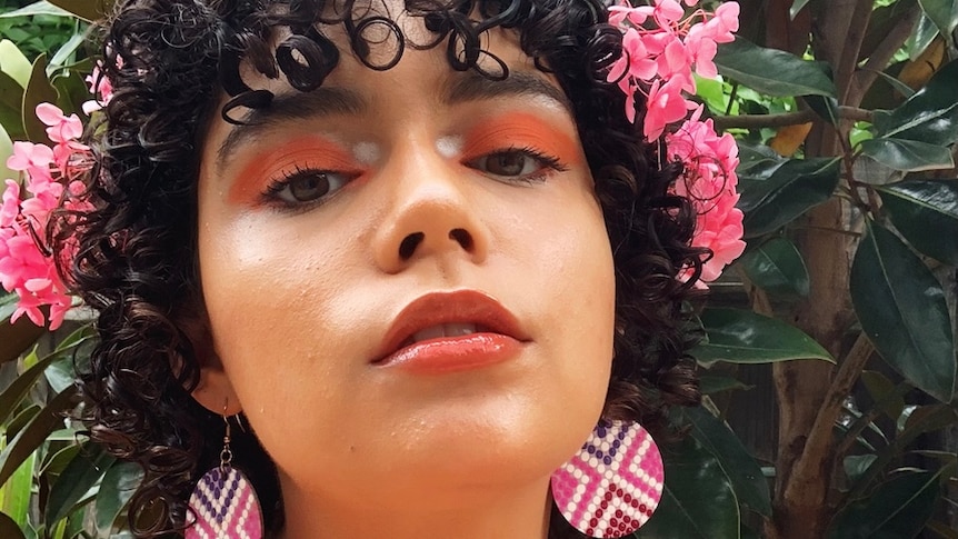 A close-up profile photo of a woman in pink earrings and flowers in her hair, in story about using the term BIPOC.