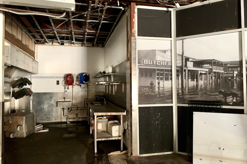 An empty room with a historic mural of a butchery, steel benches and exposed roofing.