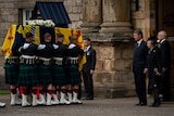 Pallbearers in kilts carry the Queen's coffin through the arches of a great stone palace.