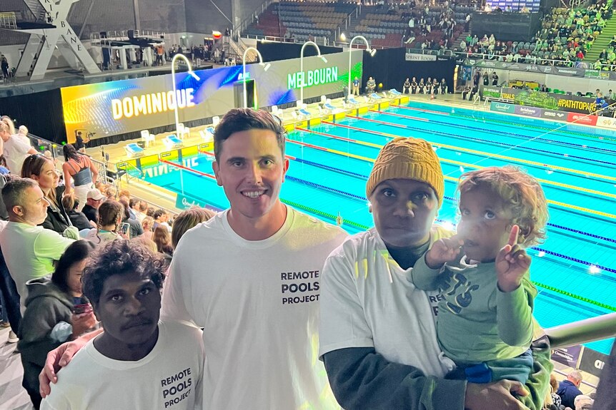 Three adults and one child stand in front of a  '2024 Australia Swimming Trials' sign.