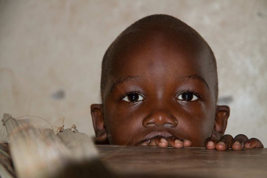 A young African child peers over a table top.