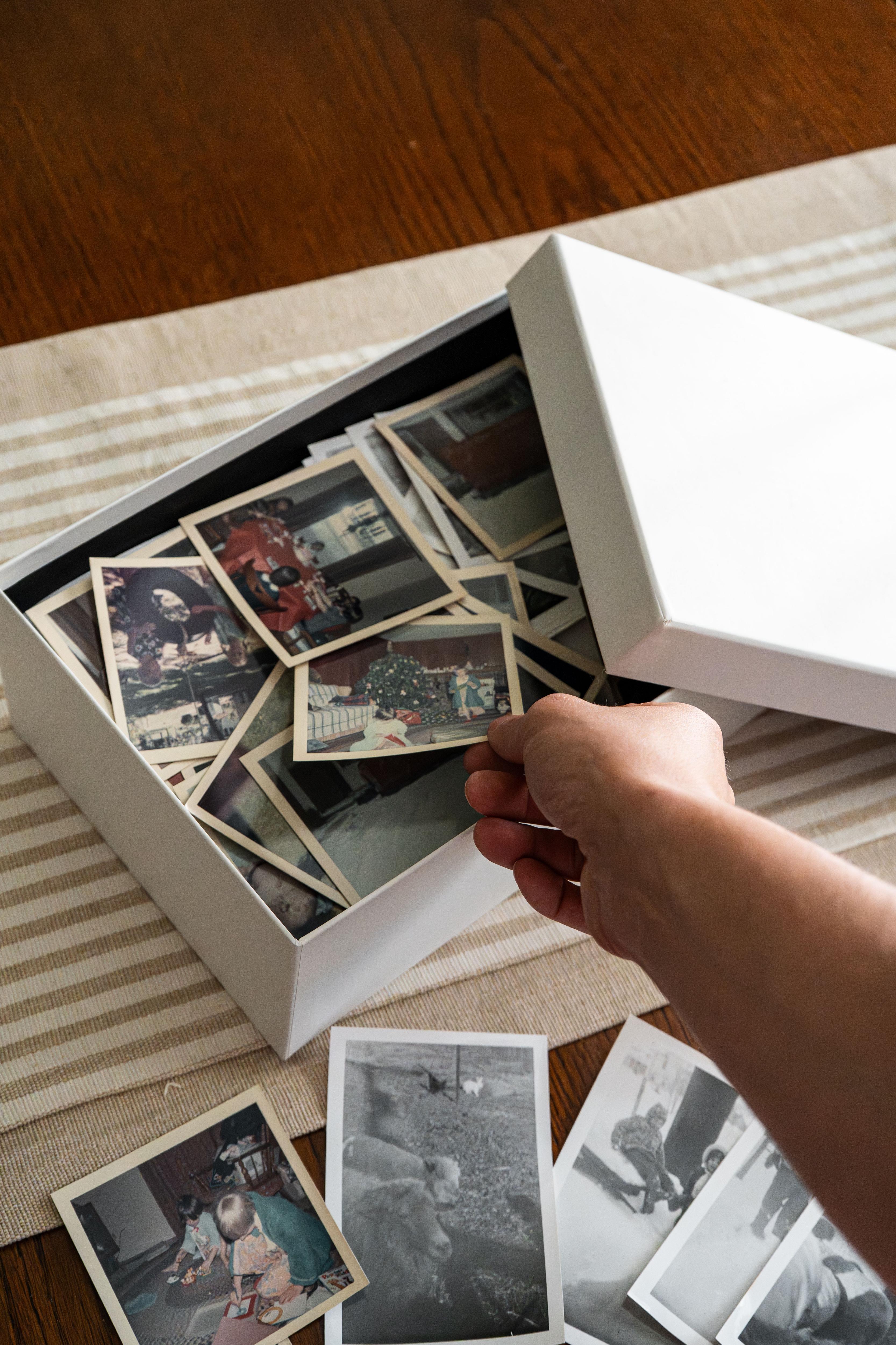Image of someone reaching inside a shoe box/memory box filled with old photos.