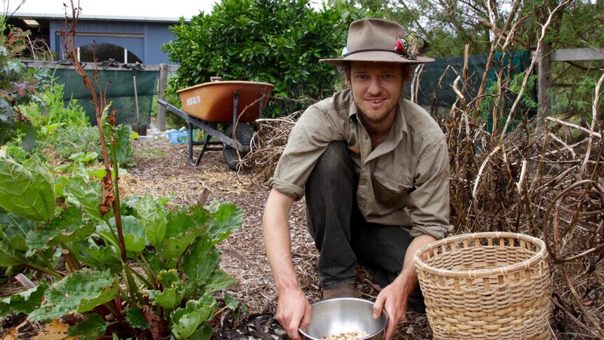 A man with a bowl of produce kneeling in a vegetable garden.