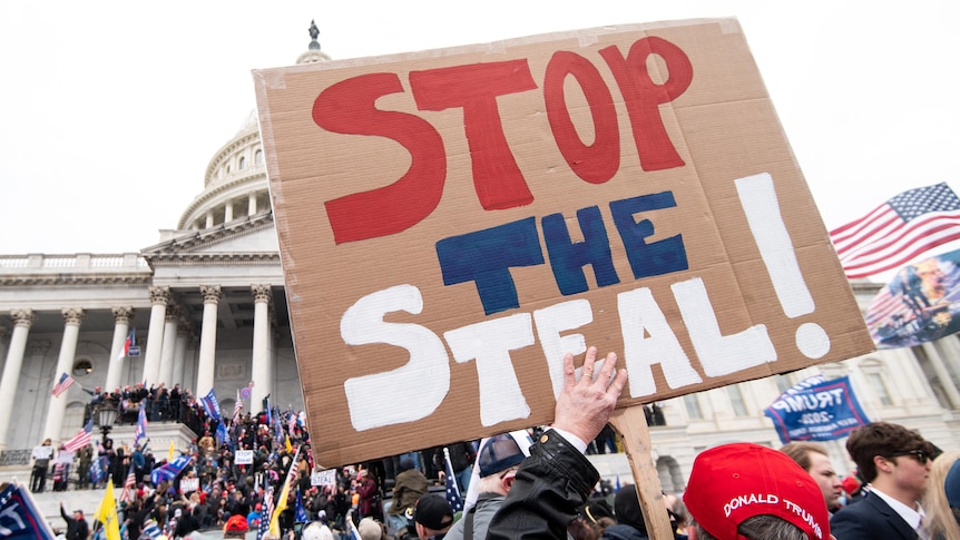 A man holds a 'stop the steal' sign in front of a US government building.