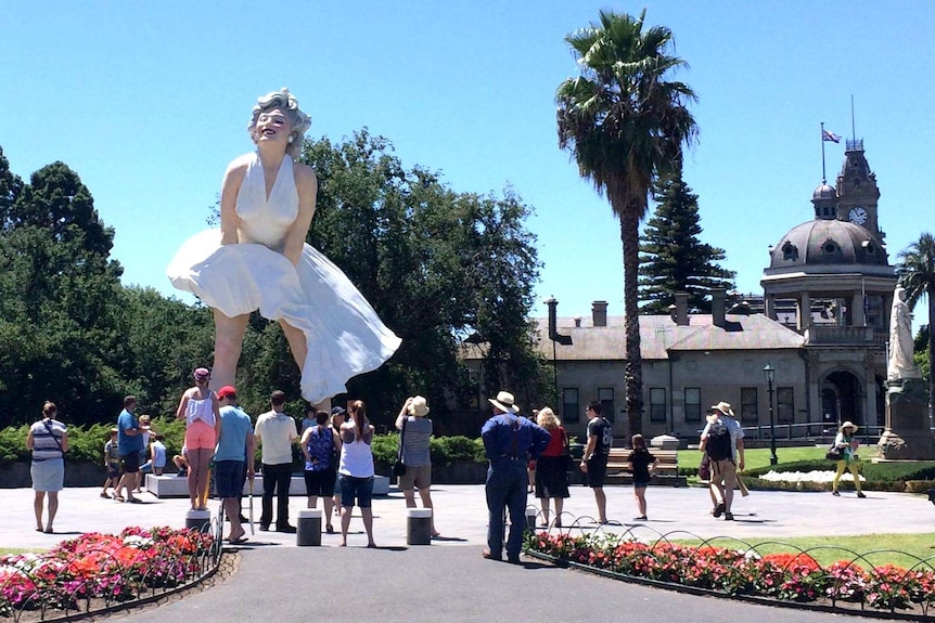 People look at a three-storey statue of Marilyn Monroe, erected in a town square.