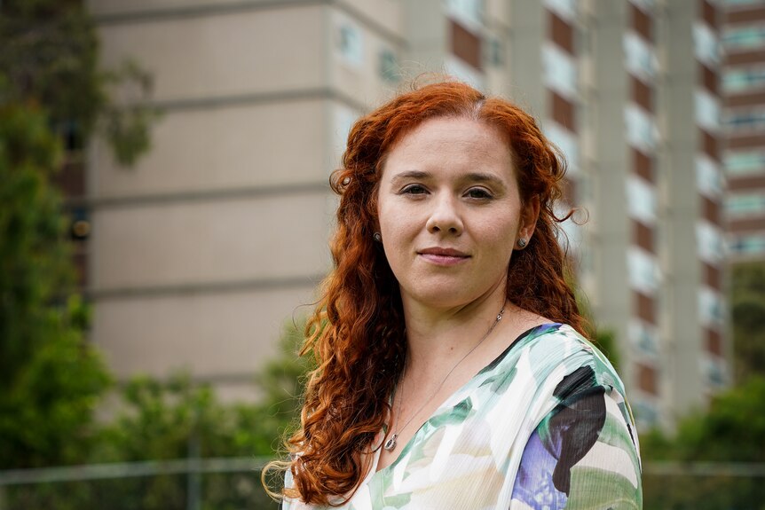 A woman with red hair poses for a portrait, with public housing towers in the background