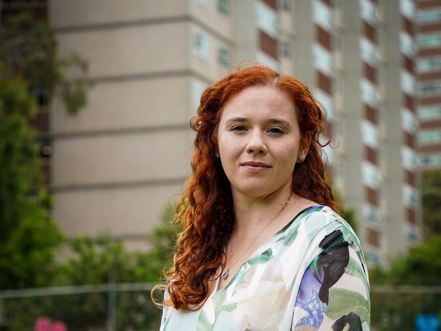 A woman with red hair poses for a portrait, with public housing towers in the background