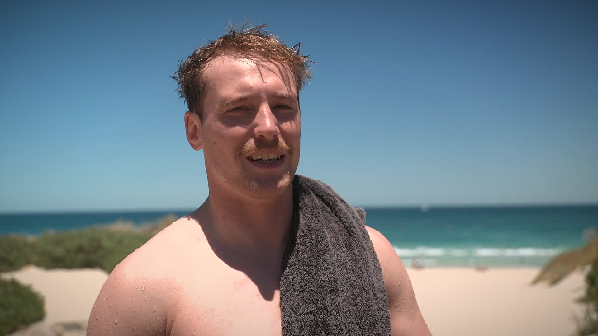 Kern está de pie en la arena con una toalla al hombro.